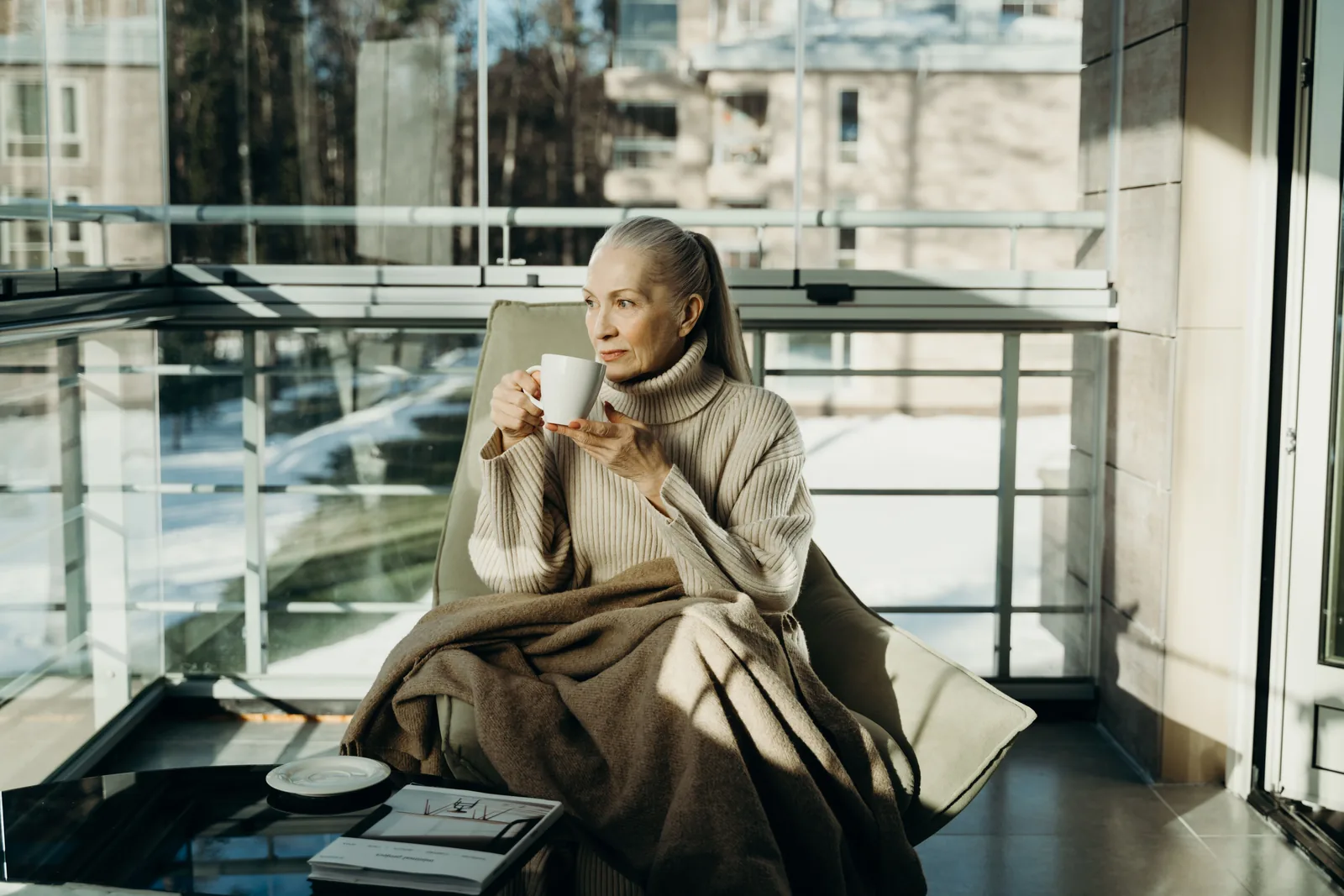 Frau sitzt nachdenklich mit einer Tasse Tee am Fenster